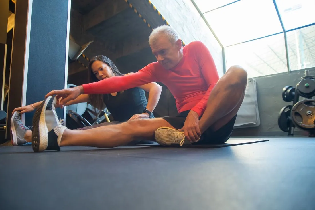 Un homme âgé s’étire au sol, accompagné par une coach