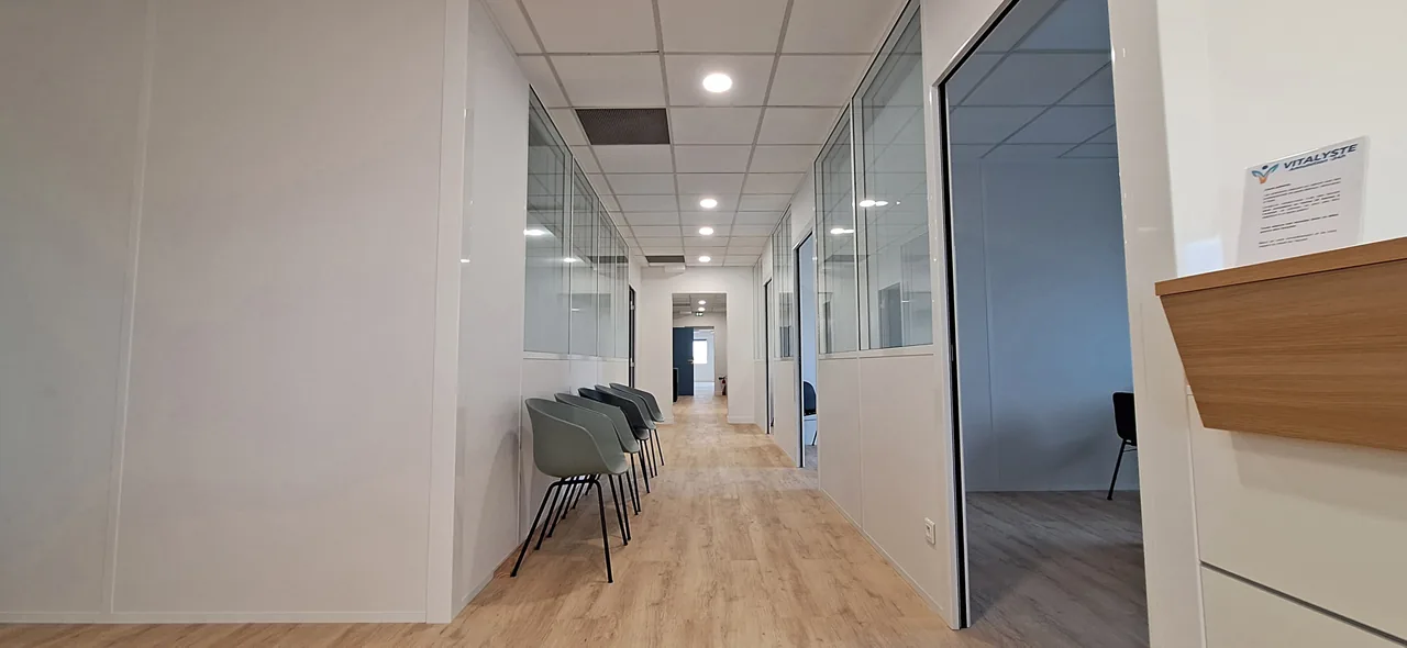 Couloir desservant les salles de soins, avec des chaises pour patienter.