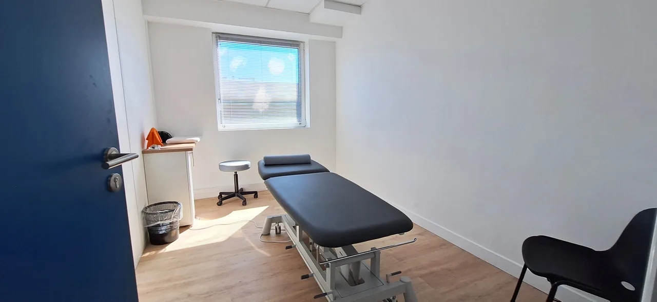 Salle de soins individuelle avec table de kinésithérapie et fenêtre.
